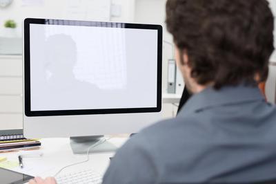 Rear view of a man sitting in front of his computer monitor on a desk, presumably about to complete a DUI class