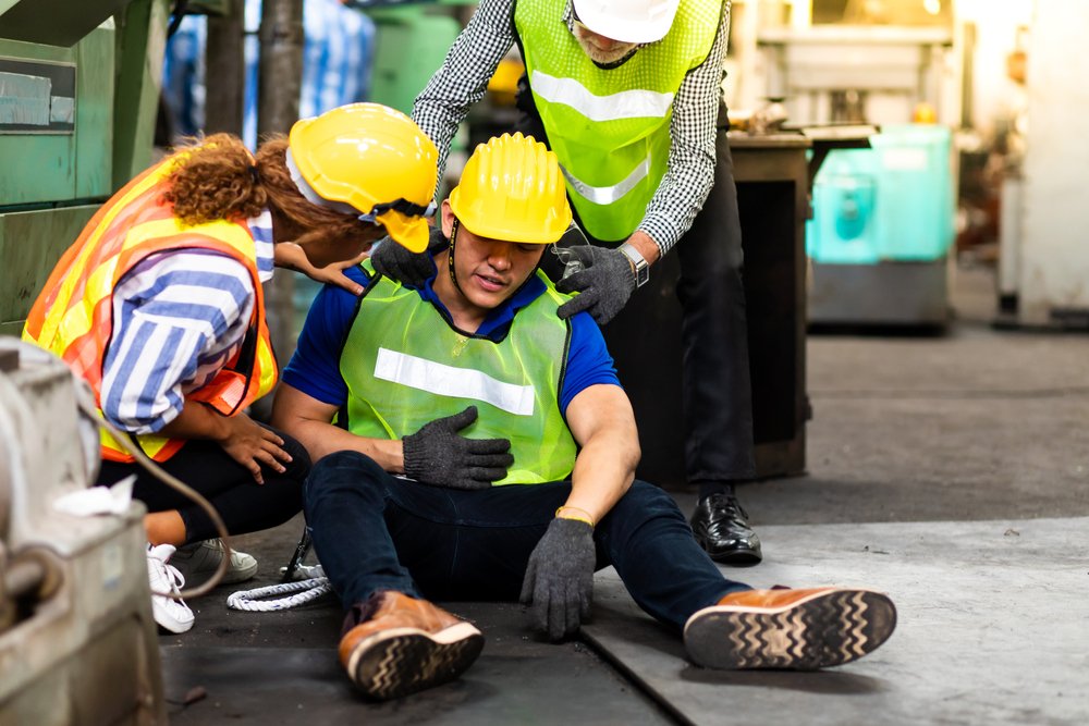 A construction worker in a hard hat lying on the ground after being badly injured while two colleagues tend to him